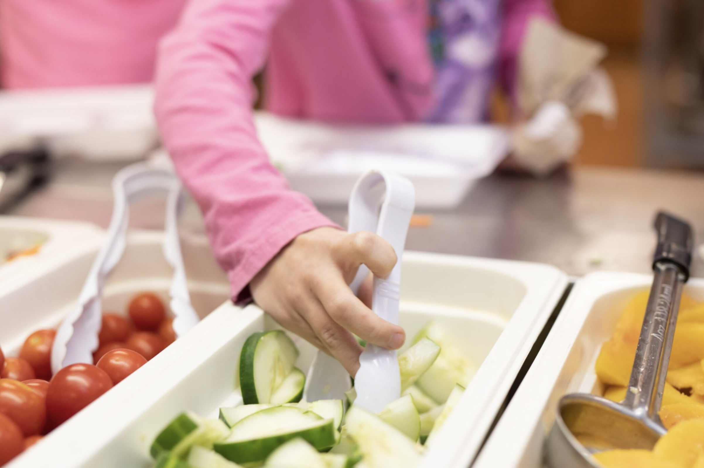 A student chooses cucumbers from the school salad bar.